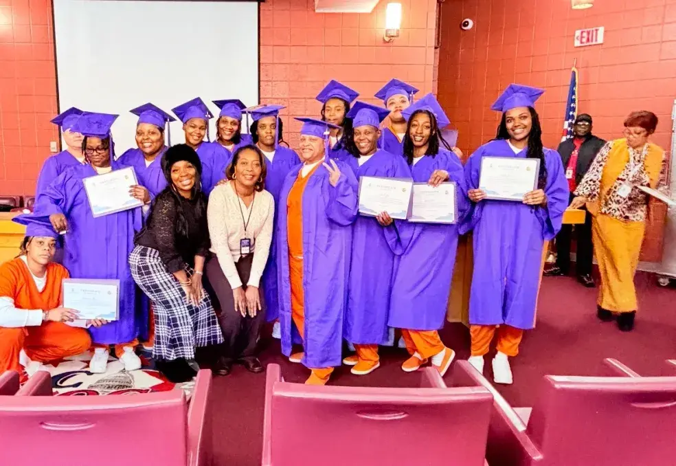 Women in purple caps and gowns celebrating their S.T.A.N.D. Program graduation while incarcerated